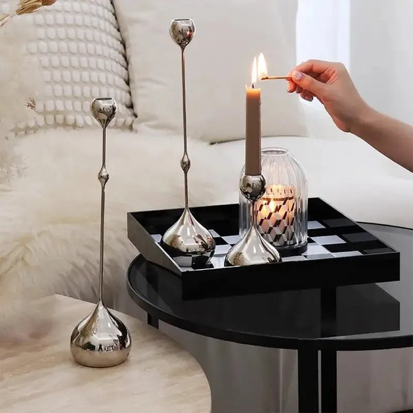A set of three silver waterdrop design candle holders with a lit candle on a black tray