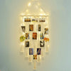 A bohemian macrame photo display featuring multiple framed photos hanging from a string on a light blue wall.