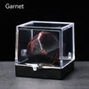 A dark garnet crystal rough stone specimen displayed inside a clear glass box.