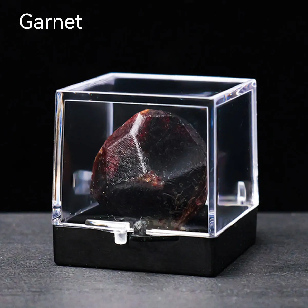 A dark garnet crystal rough stone specimen displayed inside a clear glass box.