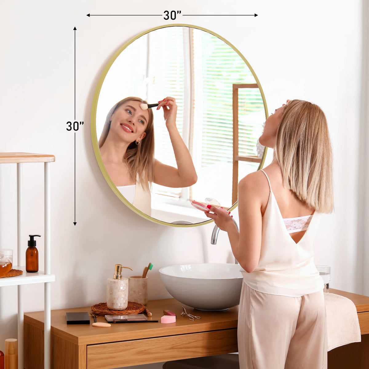 A woman is looking in a large round vanity mirror with a matte metal frame in a bathroom setting.