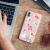 A pink smartphone displays a watercolor sticker pack featuring various animals and objects on a wooden table next to a laptop