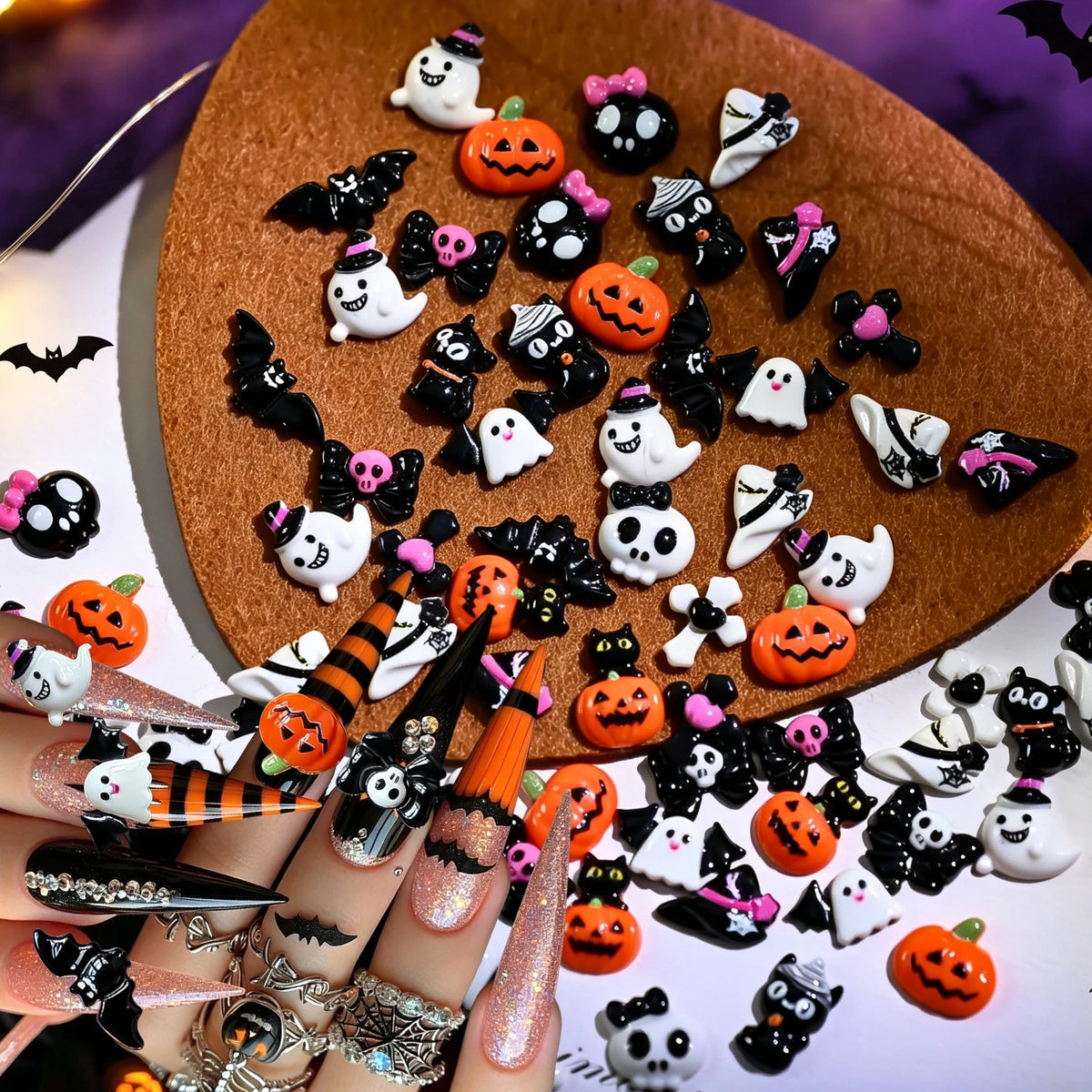 A variety pack of 50 Halloween resin nail charms featuring spooky characters like ghosts, bats, and pumpkins on a brown surfa