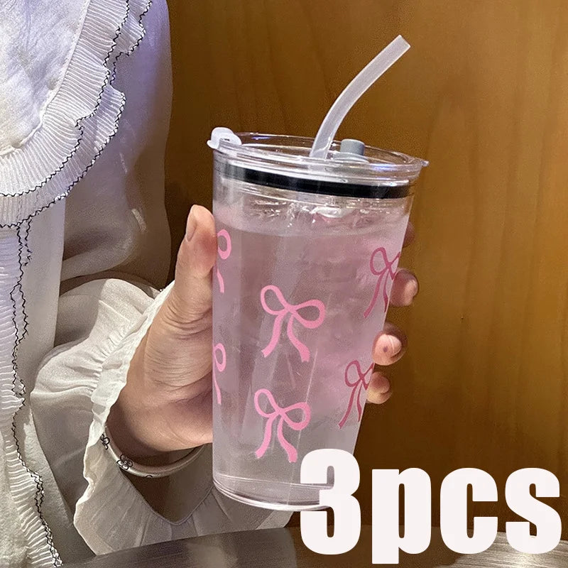 Three pink bow plastic cups with straws and lids are held in a hand against a wooden background.