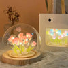 A clear glass globe night light featuring glowing pink and yellow LED tulips on a wooden base.