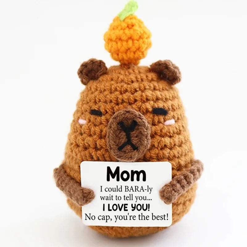 A handcrafted crochet bear doll with an orange fruit on its head, featuring a tag that reads I love you Mom.