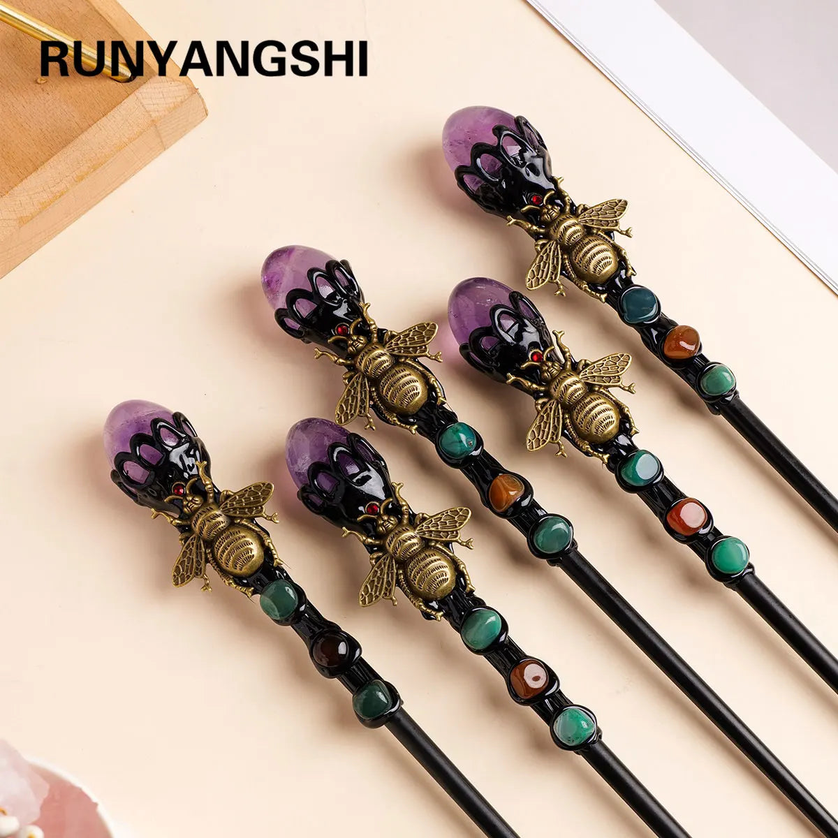 A set of five dark and purple amethyst bee crystal scepters with gold accents displayed on a light background.