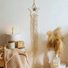 Boho macrame dream catcher wall decor featuring a star shape and long fringe hanging on a white wall.