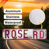 Vintage Retro Metallwand-Schild mit der Aufschrift ROSE RD vor einer Straßenkulisse.