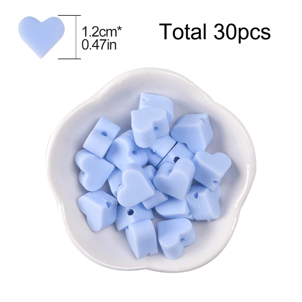 A collection of light blue silicone heart beads in various shapes is displayed in a white dish.