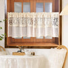 Beige sheer curtain with floral embroidery hanging in a wooden window frame.