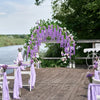 An outdoor wedding setup featuring a wooden deck decorated with purple and white floral garlands and chairs.