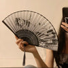 A person holds an elegant floral bird print bamboo folding fan against a light background.