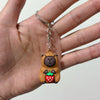 Un petit pendentif de clé USB en forme de capybara brun rond avec des feuilles vertes et une fraise rouge est tenu dans la ma