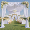A white fabric backdrop curtain decorated with floral garlands and draped fabric for an outdoor event.