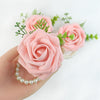A hand holds an elegant wrist corsage bracelet featuring pink silk roses and green foliage.