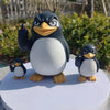 A desk statue of a black and white penguin with one flipper raised, standing on a white base.