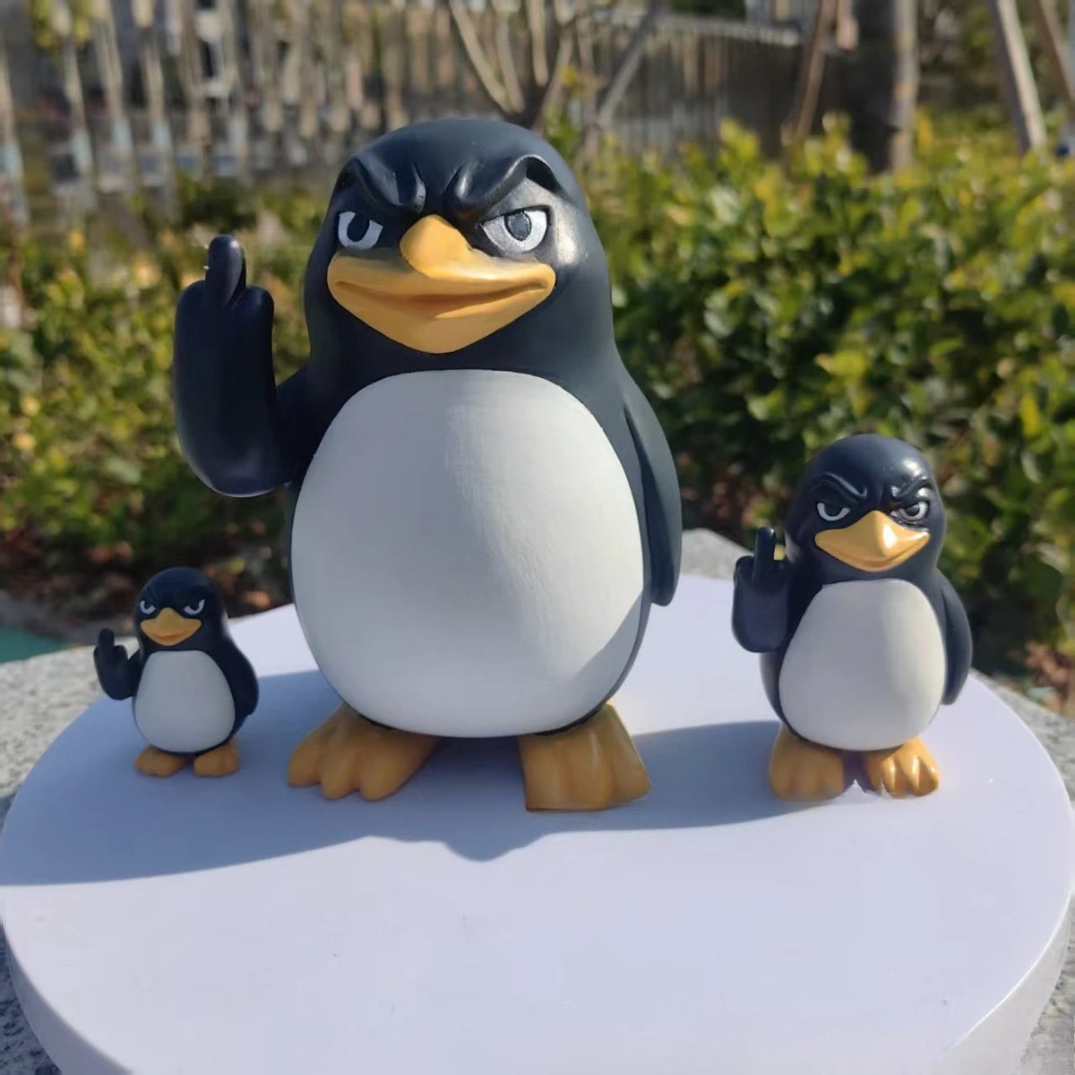 A desk statue of a black and white penguin with one flipper raised, standing on a white base.