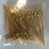 A clear plastic bag filled with numerous bamboo fruit skewers featuring gold-colored spherical tops.