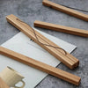 A wooden poster hanger with a teak finish is shown resting on white paper against a gray background.