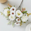 A bouquet of artificial white and cream silk flowers with green foliage and dried accents on a white surface.