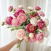 A hand holds a bouquet of lifelike silk peony flowers in shades of pink and white.