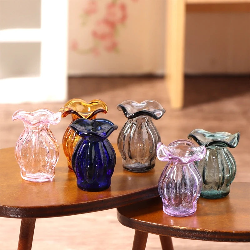 A set of miniature glass vases and wine bottles in various colors displayed on a wooden table.