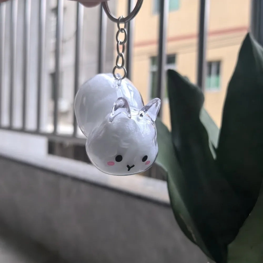 A clear, round rabbit charm hangs from a silver chain against a blurred background.