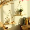 Two macrame wood floating wall shelves with hanging rope displaying plants and decorative items on a light-colored wall.