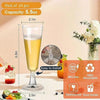 A set of disposable champagne glasses with a gold finish is shown next to an orange juice and flowers.