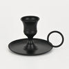 A black artisan metal candle holder with a flared cup and a circular handle.