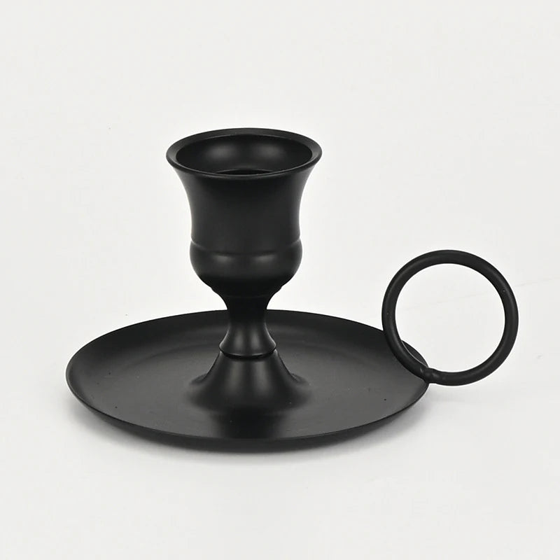A black artisan metal candle holder with a flared cup and a circular handle.