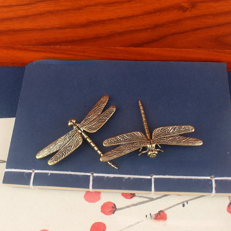 Vintage brass dragonfly desk decor resting on a dark blue coaster.