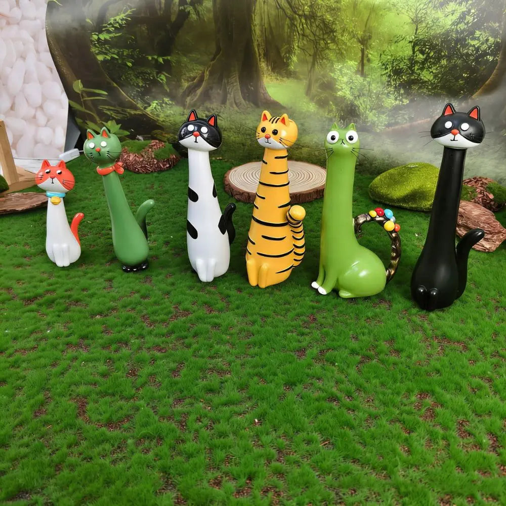 A collection of cat-shaped resin figurines in various colors and patterns displayed on green grass against a forest backgroun