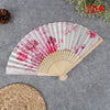 A hand carved bamboo folding fan with pink and green floral patterns resting on a gray surface.