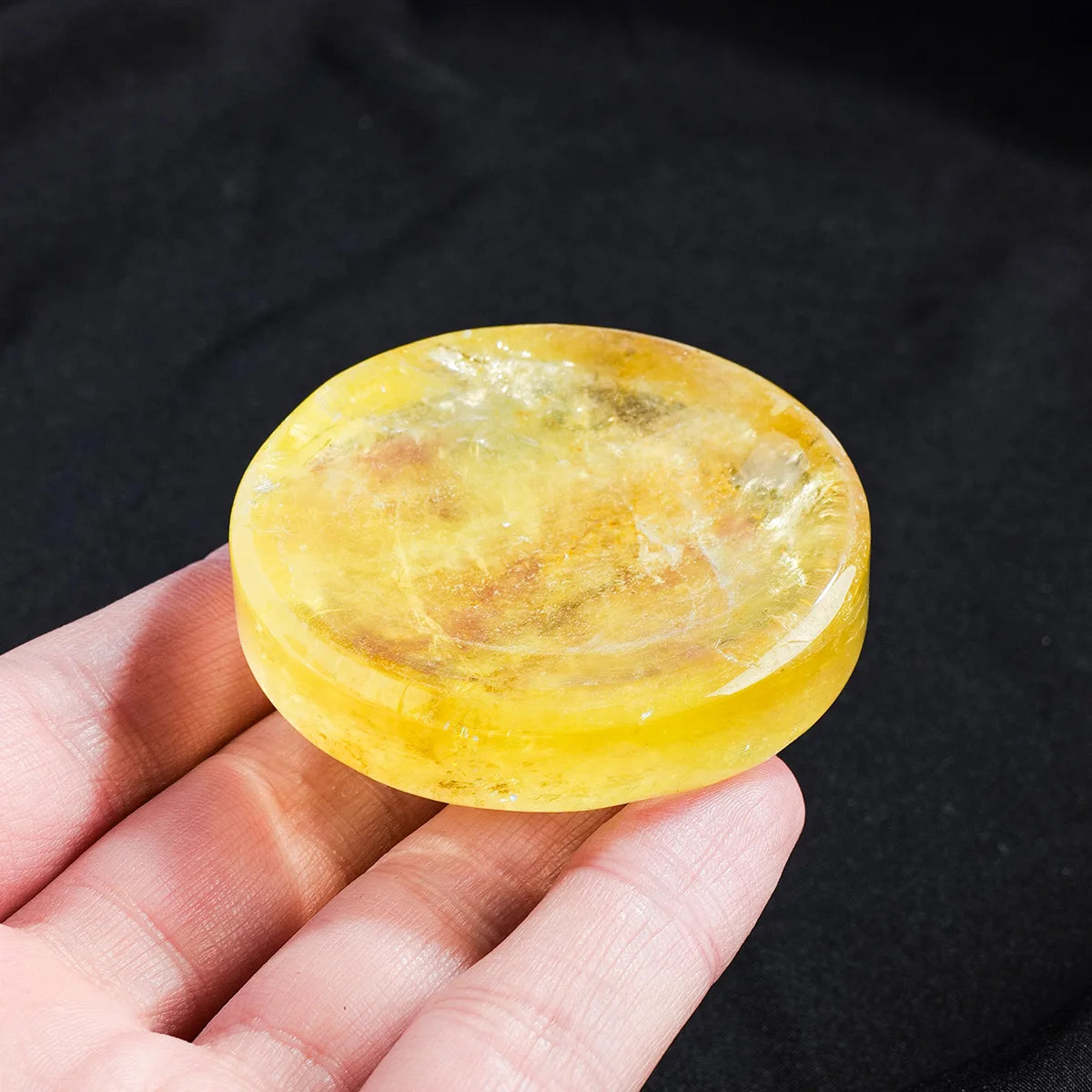 A hand holds a smooth, oval yellow citrine crystal bowl for meditation and decor.