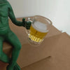 A resin statue of a green alien holding a glass of beer on brown cardboard.
