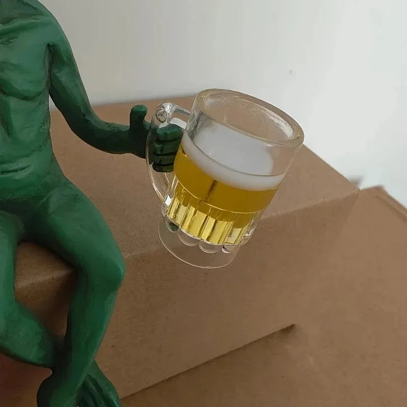 A resin statue of a green alien holding a glass of beer on brown cardboard.