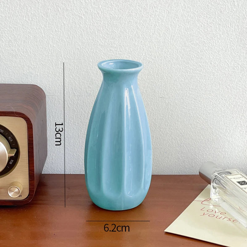 A light blue ceramic bud vase is shown on a wooden surface next to a vintage-style radio.