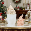 A pink silicone candle mold shaped like a gnome with a honeycomb hat, displayed on a white ceramic holder.