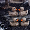 A collection of small, realistic resin duck figurines with detailed feathers and orange beaks resting on dark gravel.