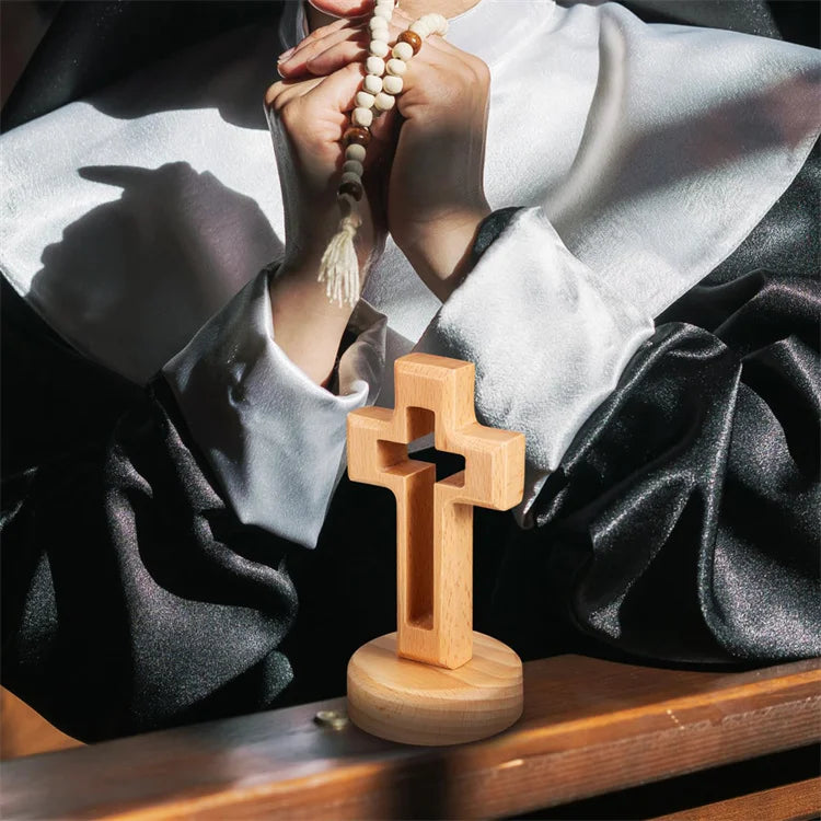 A wooden crucifix wall ornament is held by hands against a draped cloth.