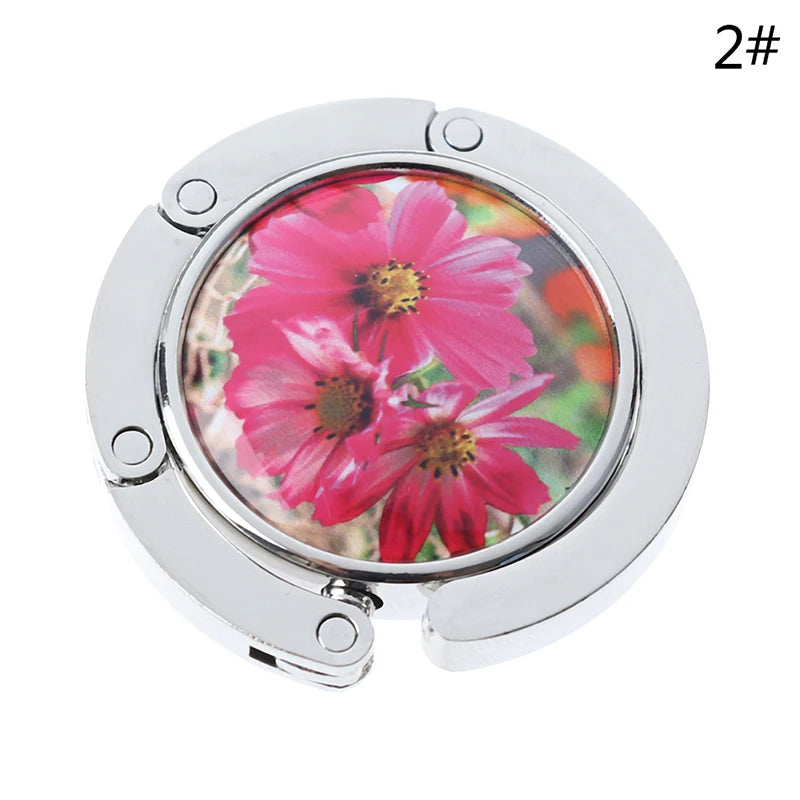 Silver foldable handbag hook with a pink flower design for securing items on tables and desks