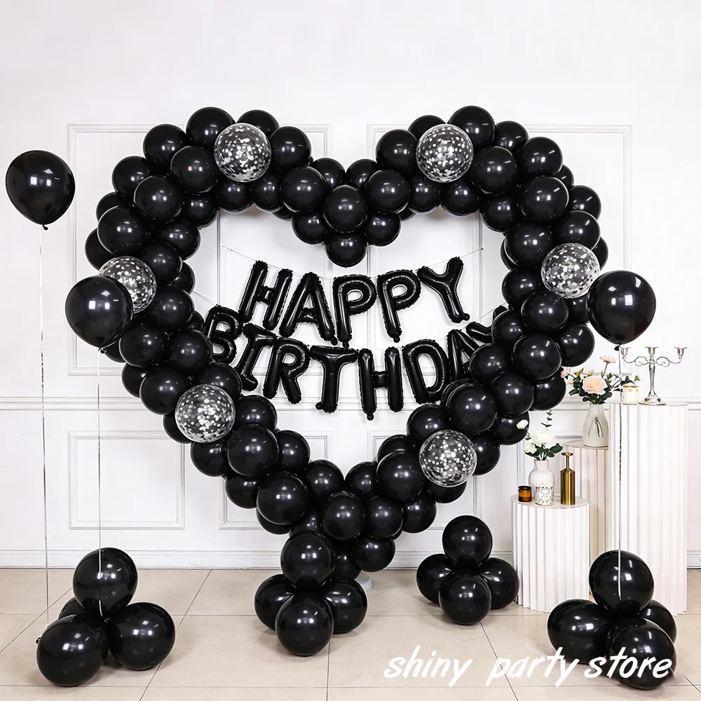 A heart-shaped balloon arch made of black latex balloons spelling out Happy Birthday