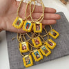 Hand holding a gold-plated charm bracelet featuring small religious figures on yellow fabric charms.
