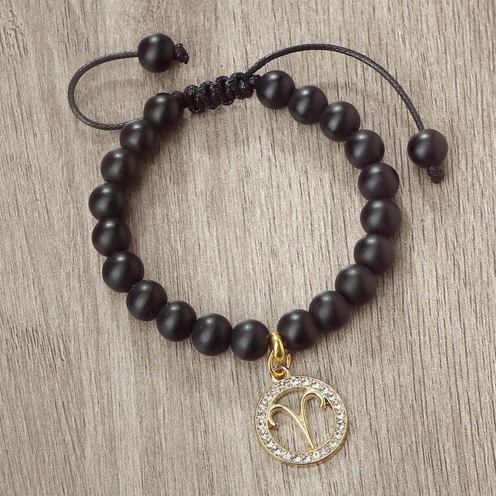 A handmade beaded bracelet featuring natural black stones and a gold zodiac charm.
