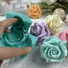 Hand holding a teal silicone mold shaped like a rose flower, surrounded by other colored silicone floral molds.