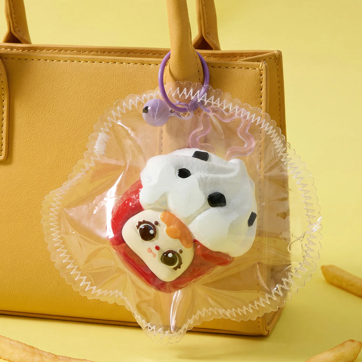 A clear plastic pouch containing a white and red collectible squeeze toy keychain attached to a tan leather handbag.