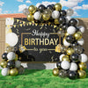 A balloon garland arch featuring black, gold, and white balloons with starburst accents set against a dark backdrop.