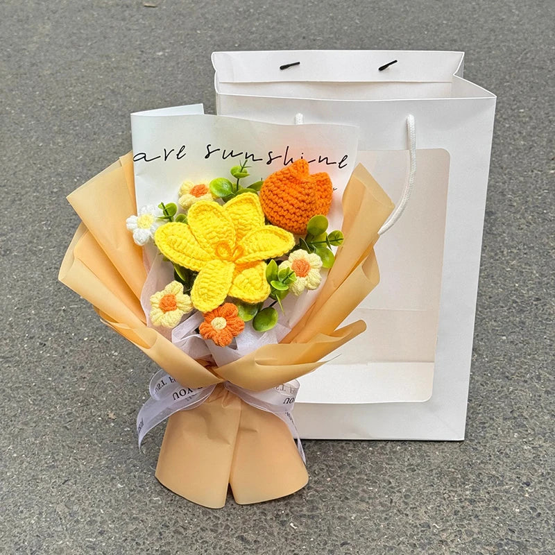 A bouquet of handmade crochet flowers in yellow and orange sits inside a light brown paper bag.